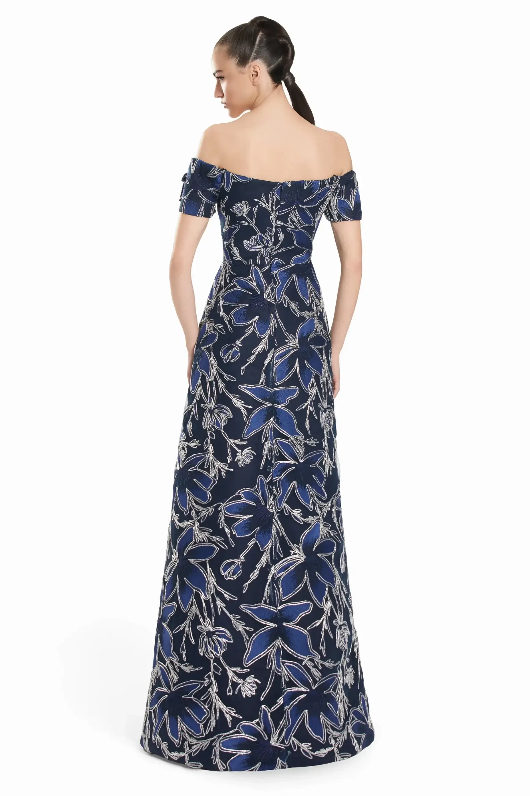Model is wearing a regal navy and silver off-the-shoulder A-line gown with bold floral embroidery.
