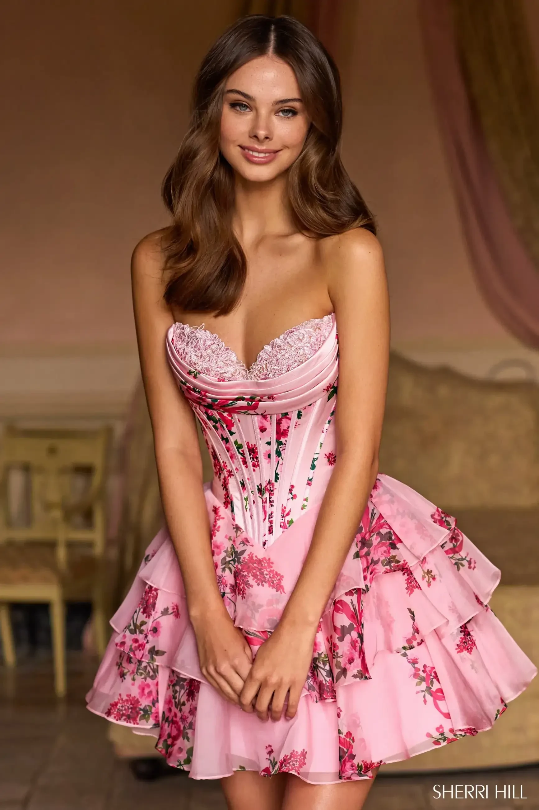 Model is wearing a floral strapless cocktail dress with a satin corset bodice and a chiffon ruffle skirt.