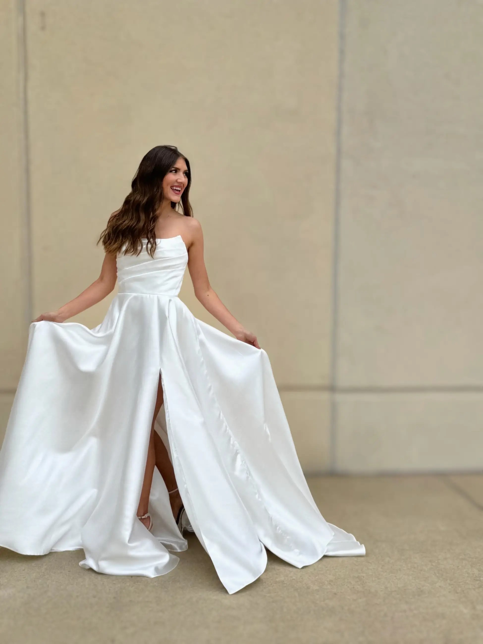 model is smiling and wearing a strapless a-line wedding dress with a thigh high slit
