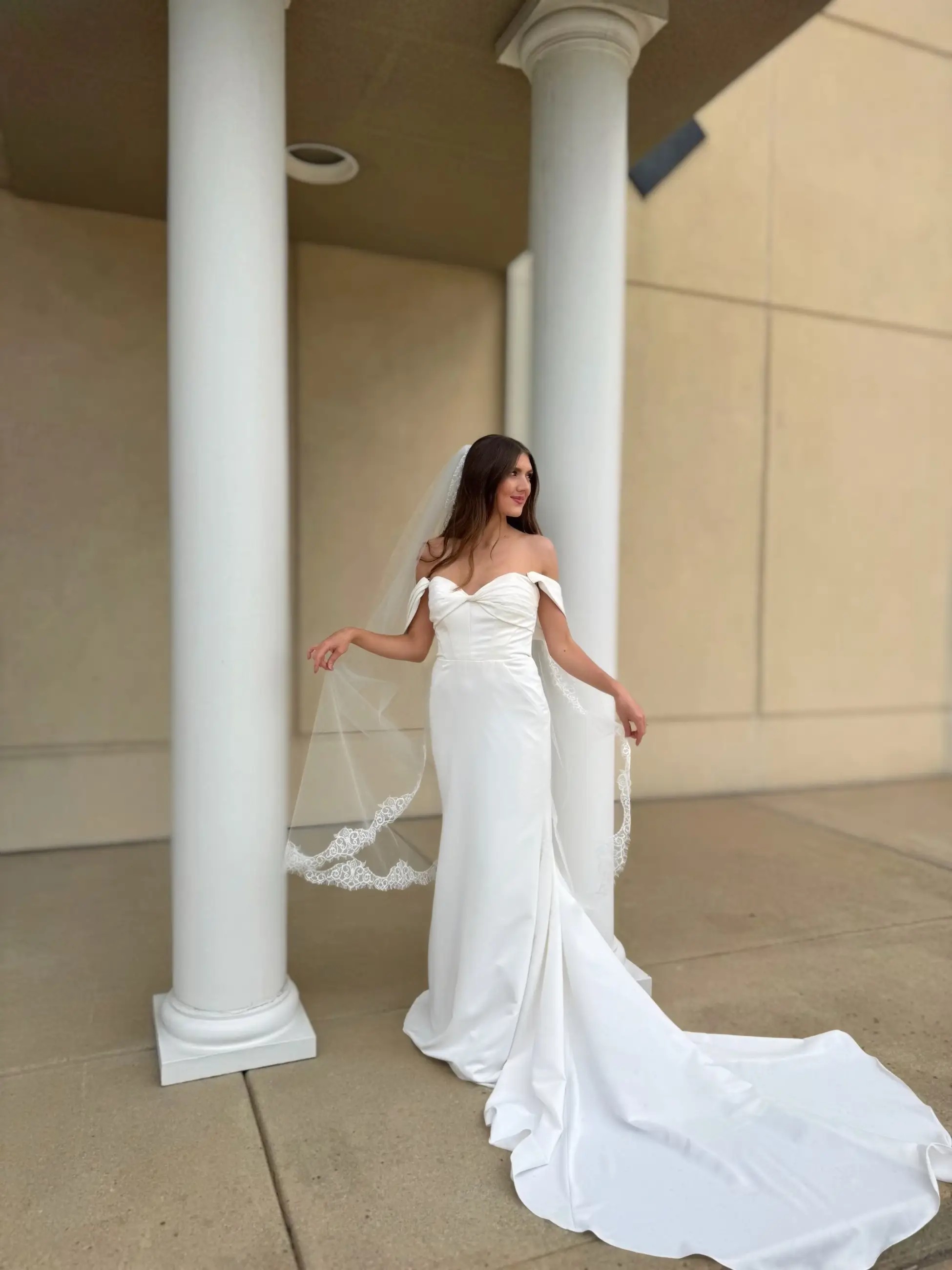 model is wearing an off the shoulder wedding dress with a long train and sweetheart neckline